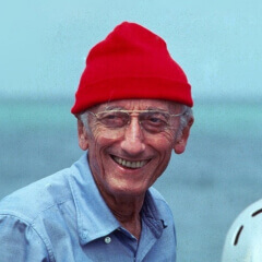 A portrait photo of Jacques-Cousteau with red beanie and the ocean in the background